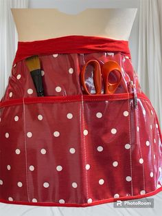 a woman's red polka dot apron with scissors and hairbrushes in it