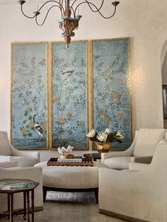 a living room filled with furniture and a chandelier hanging from the ceiling next to two paintings