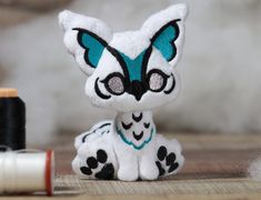 a small white and black cat sitting next to a spool of thread on top of a wooden table