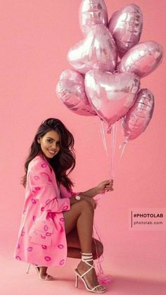 a woman sitting on a chair holding some pink balloons