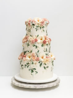 a three tiered wedding cake with flowers on the top and bottom, sitting on a platter