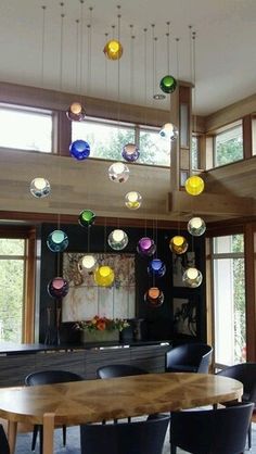 a dining room table with chairs and lights hanging from it's ceiling in front of large windows