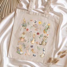 an embroidered tote bag with cats and flowers on it next to some straws