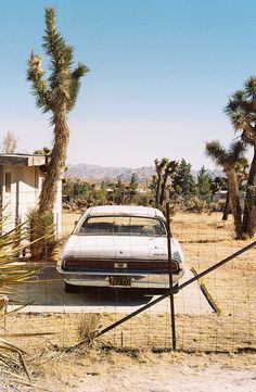 an old car is parked in front of a house with palm trees and a fence