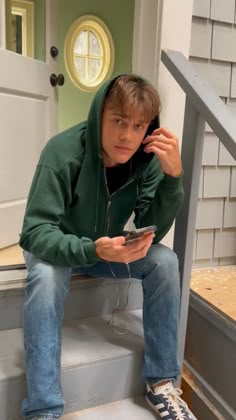 a young man sitting on the steps while listening to his cell phone with ear buds in his ears