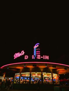 people are walking in front of a building with neon lights on it at night time