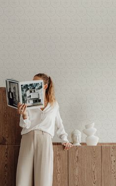 a woman standing in front of a wall holding an open magazine