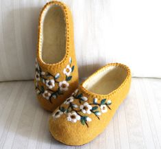 a pair of yellow slippers with white flowers on them sitting on top of a couch