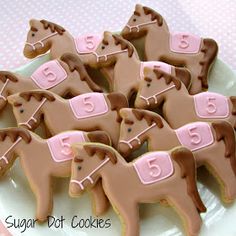 some cookies are shaped like horses on a white plate with pink trimmings and numbers