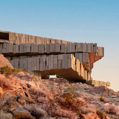 a concrete structure sitting on top of a rocky hill next to dry grass and bushes