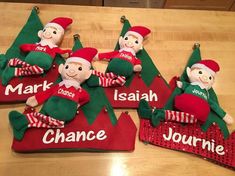 four elf ornaments with names on them sitting on a wooden table next to each other