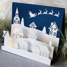 a paper cut christmas scene with santa's sleigh flying over the town