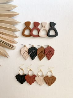 four pairs of leaf shaped earrings on a white surface with palm leaves in the background