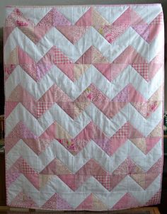 a pink and white quilt hanging on a wall