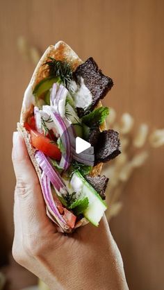 a person holding a sandwich with meat and vegetables