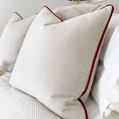 three white pillows with red piping sit on a bed