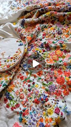 a bed covered in lots of colorful flowers next to a white pillow with an embroidered cover over it