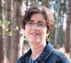 a woman wearing glasses standing in the woods