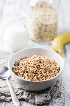 a white bowl filled with granola next to a banana