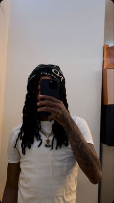 a man with dreadlocks taking a selfie in front of a mirror wearing a hat