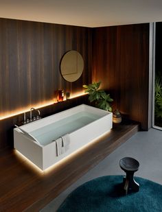 a bath tub sitting on top of a wooden floor next to a mirror and potted plant