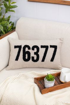 a white couch with a wooden tray holding a coffee cup and potted plant on it