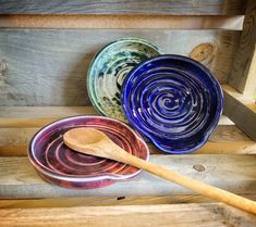 three bowls and a wooden spoon sitting on top of a bench with wood slats