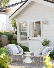 two wicker chairs sitting in front of a white house with a door and window