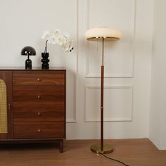 a floor lamp next to a dresser with flowers on it