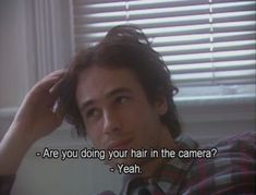 a man sitting in front of a window holding his hair up to his head with the words are you doing your hair in the camera? yeah