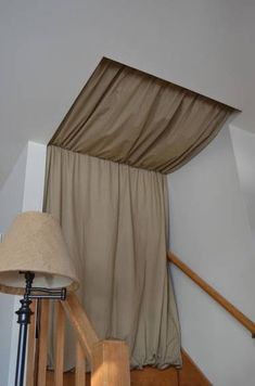 a lamp is sitting next to a curtain on the stair case in a house with white walls and wood floors