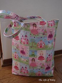 a pink and green bag with princesses on it sitting on the floor next to a wall