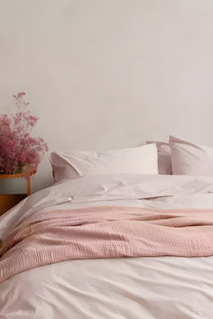 a bed with white sheets and pink flowers in a vase on the nightstand next to it