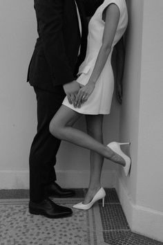 a man and woman kissing in front of a wall with their feet on the ground