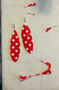 two red and white polka dot earrings on a piece of fabric next to some scissors