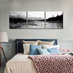 three black and white paintings on the wall above a bed with pillows, blankets and lamps