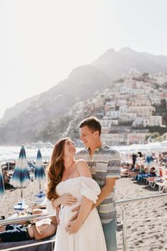 a man and woman standing next to each other on a beach with umbrellas in the background