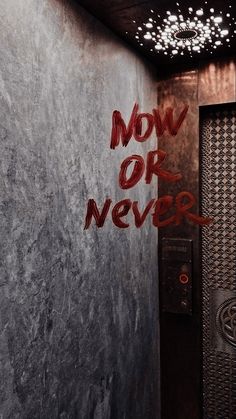 the word now or never is spray painted on the wall next to an elevator door