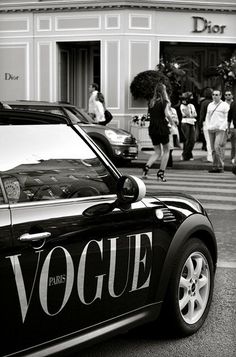 a black and white photo of a car parked on the side of the road with people walking by