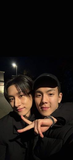 two young men standing next to each other in front of a street light at night