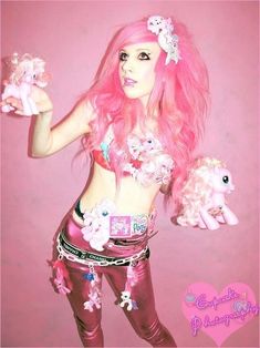 a woman with pink hair holding two ponies in one hand and a stuffed animal in the other