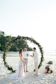 a man and woman standing on top of a beach next to an arch covered in flowers