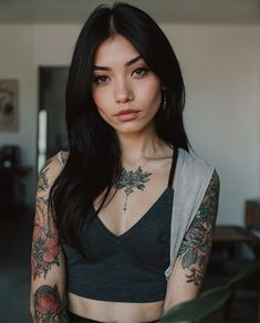 a woman with long black hair and tattoos on her arms, wearing a gray tank top