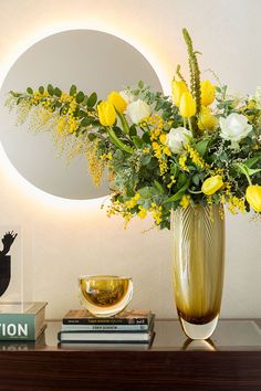 a vase filled with yellow and white flowers on top of a table next to a mirror