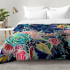 a bed covered in a colorful comforter next to a night stand