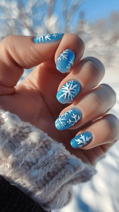 A manicured hand with icy blue nails with white snowflake designs representing Elsa from Frozen. Icy Snowflake Nails, Nail Ideas Snowflake, Snowflake Nail Art Designs, Elsa Nails Frozen, Blue Christmas Nail Art, Frozen Nails Disney, Xmas Nails Snowflake, Blue Winter Nails Short