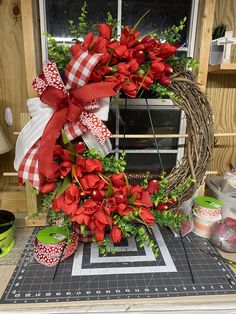 a wreath with red poinsettis and green leaves on a table next to a window