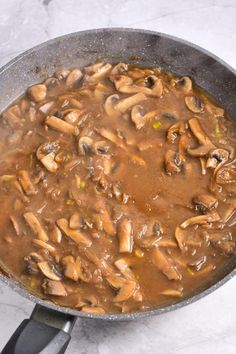 a skillet filled with mushrooms and sauce on top of a marble countertop next to a spatula