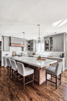 a large kitchen with an island in the middle and chairs at the end, surrounded by gray cabinets