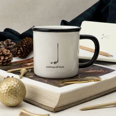 a white coffee mug sitting on top of a book next to a golden golf ball